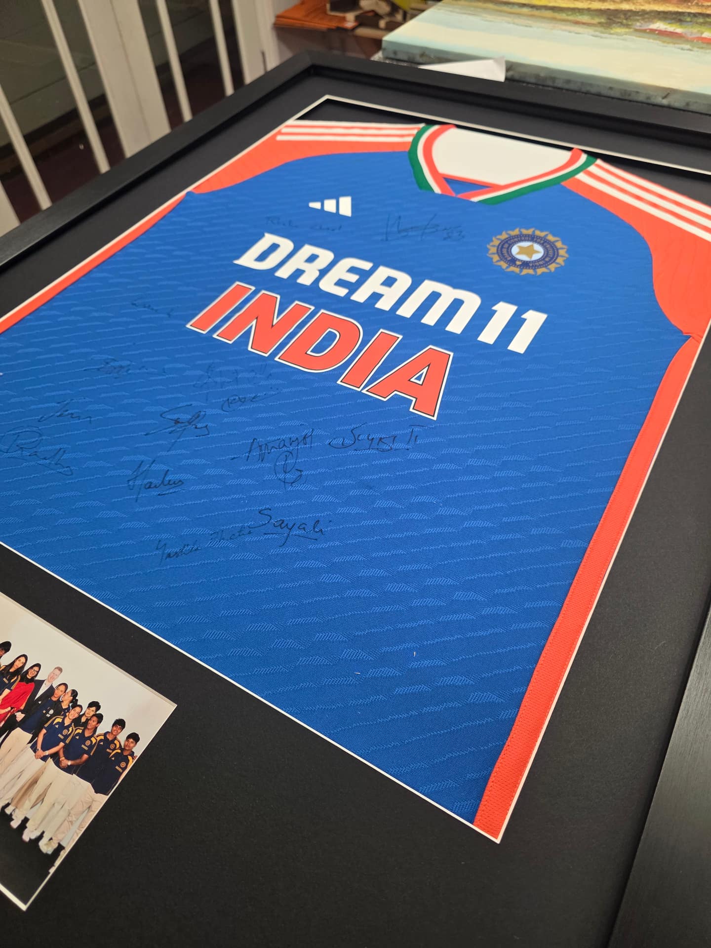 A signed team shirt mounted behind UV-protective glazing with a team photograph in a deep black frame at Love to Frame